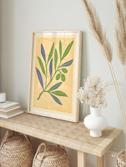 Botanical olive branch illustration with green and blue leaves on a textured yellow background, in an alternate framed mockup