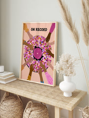 Illustrative wall art of a vinyl record surrounded by hands with ON RECORD text in pink, in an alternate framed mockup