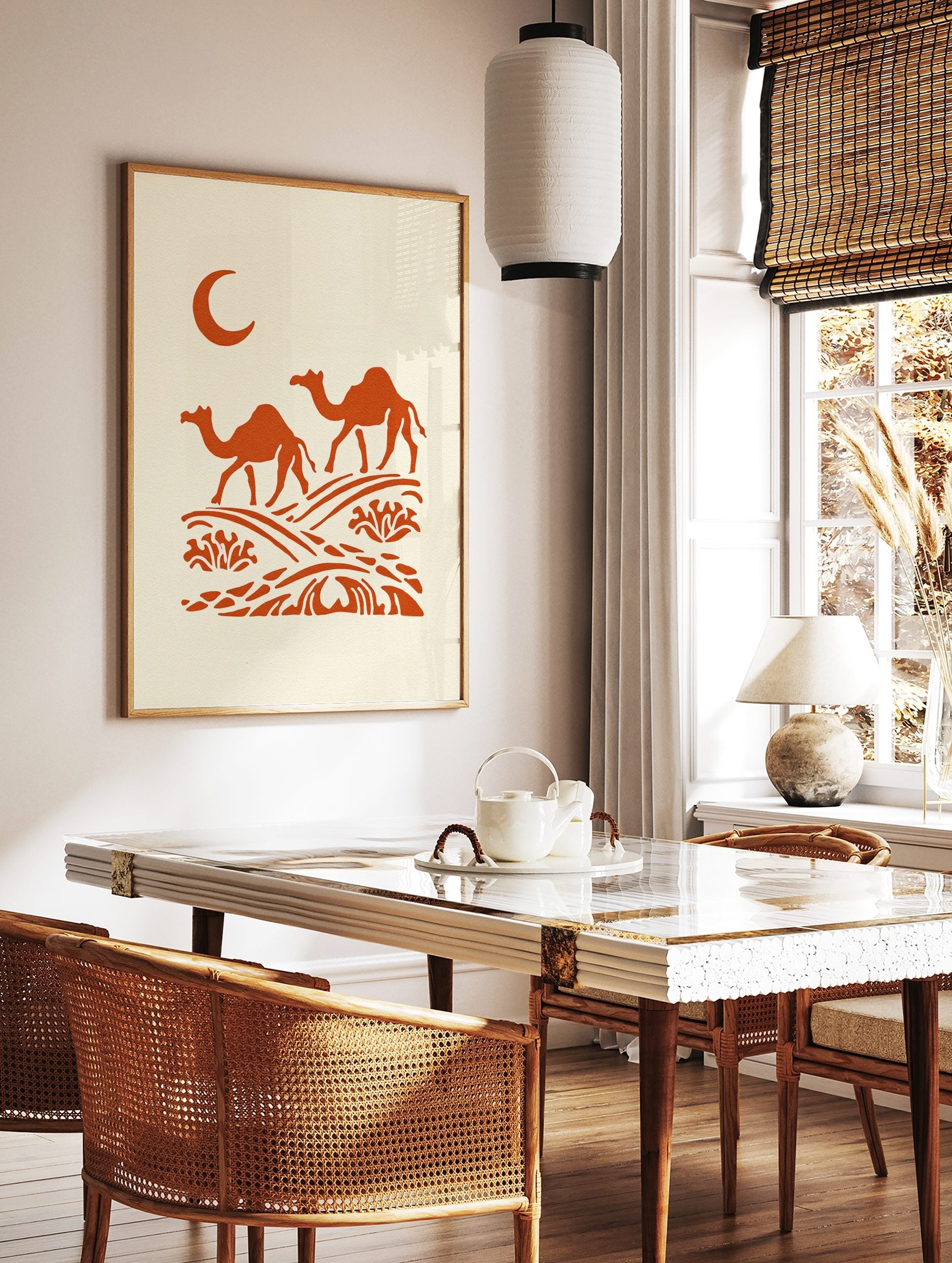 Illustrative orange dromedary camels walking on desert dunes under a crescent moon on a cream, in a styled room mockup