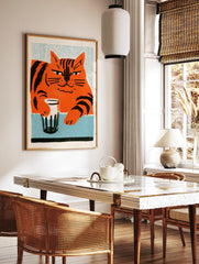 Stylised orange cat with black stripes holding a glass on a blue table, illustrative wall art print, in a styled room mockup