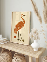 Stylized orange crane bird illustration with Japanese-style red seal on cream background, in an alternate framed mockup