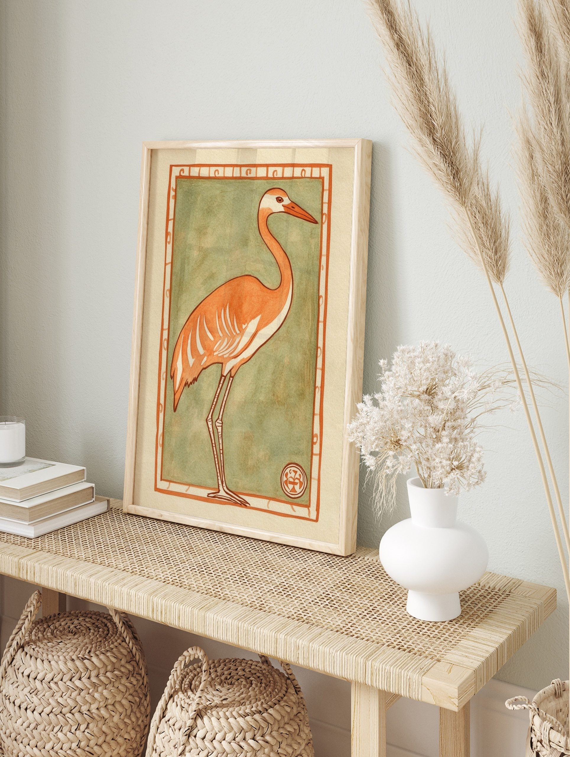 Stylised orange crane with white details and long legs, set against a sage green background, in an alternate framed mockup