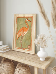 Stylised orange crane with white details and long legs, set against a sage green background, in an alternate framed mockup