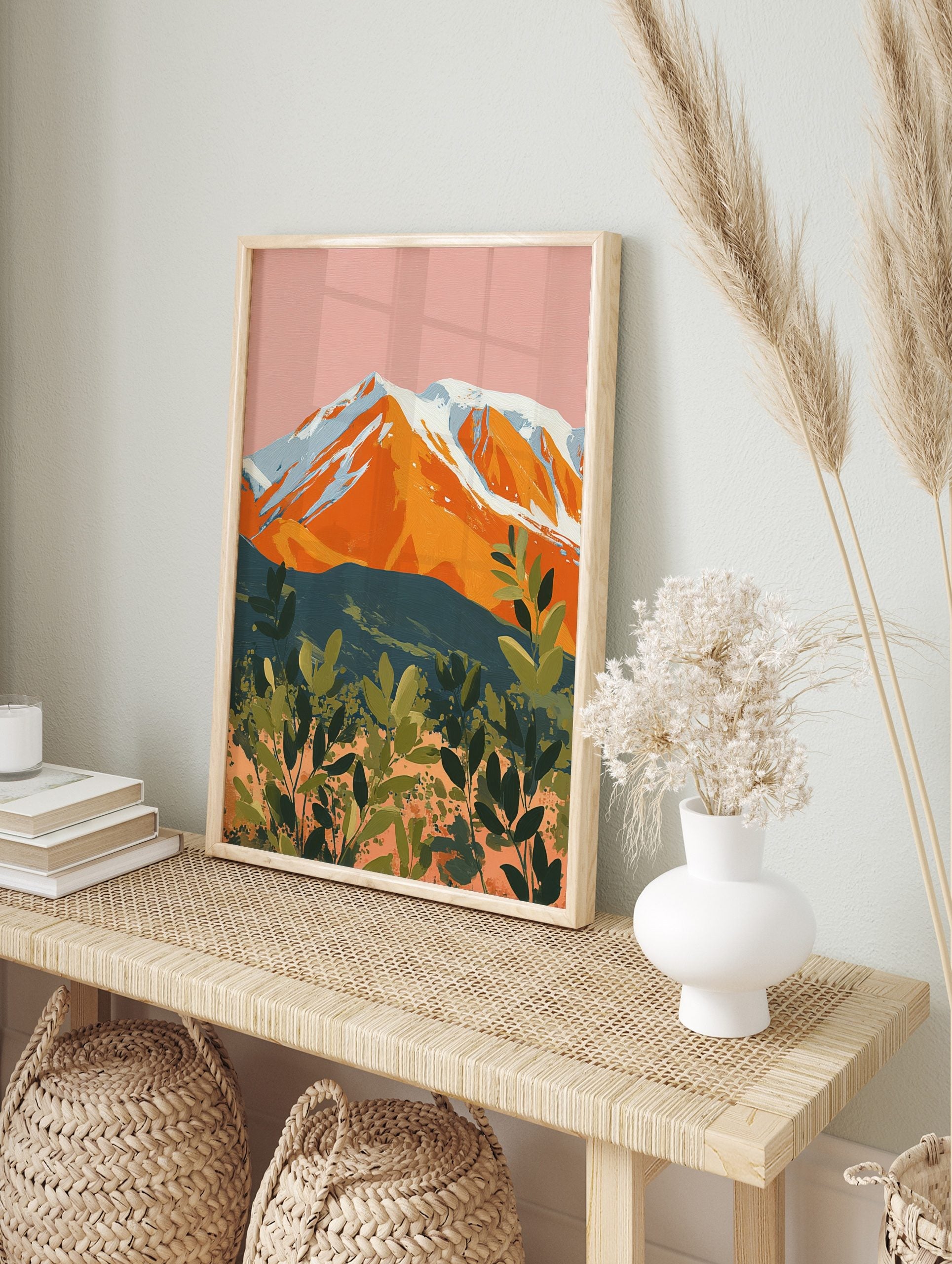 Illustrative orange mountain with snowy peaks against a pink sky and green layered foliage, in an alternate framed mockup