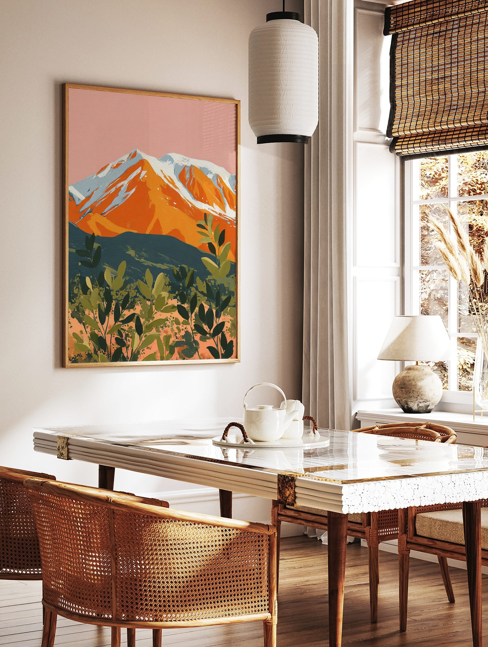 Illustrative orange mountain with snowy peaks against a pink sky and green layered foliage art print, in a styled room mockup