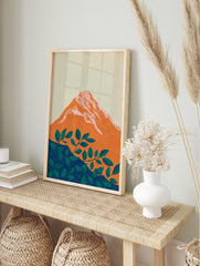 Stylised orange mountain with pink-white peaks and green foliage on a deep blue base, set, in an alternate framed mockup