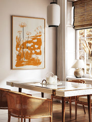 Minimalist illustrative print of white sheep and tall orange flowers in an orange field on a cream, in a styled room mockup