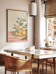 Illustrative orange still life print with fruit in a bowl, green leaves, and red berries on a, in a styled room mockup