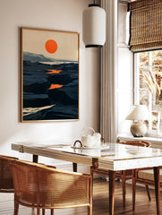 Minimalist landscape art print with a bold orange sun over a dark, rocky canyon terrain in blue and, in a styled room mockup
