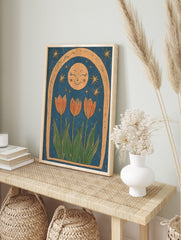 Illustrative print of three orange tulips, a smiling moon, and stars within a textured arch, in an alternate framed mockup