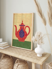 Ornate red teapot illustration with blue lid and central leaf motif, on a beige background, in an alternate framed mockup