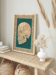 Ornate skull illustration in dark teal on beige, with intricate floral patterns and, in an alternate framed mockup