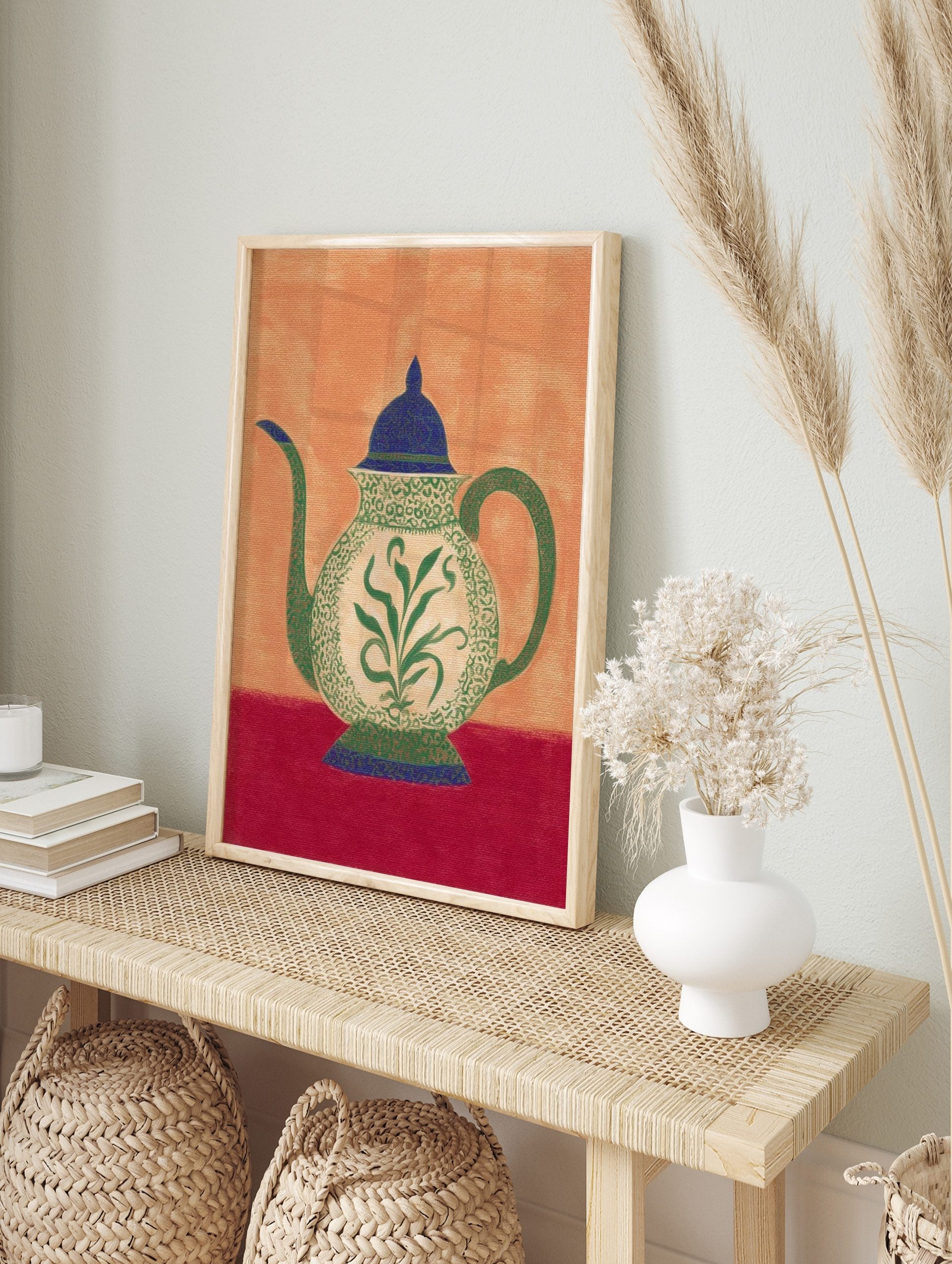 Ornate teapot illustration with green botanical pattern, blue lid, and red table on an orange, in an alternate framed mockup