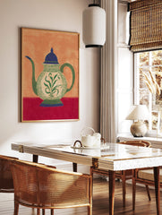 Ornate teapot illustration with green botanical pattern, blue lid, and red table on an orange, in a styled room mockup