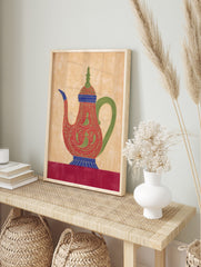 Ornate red teapot illustration with green patterns, blue accents, and a green handle on a, in an alternate framed mockup