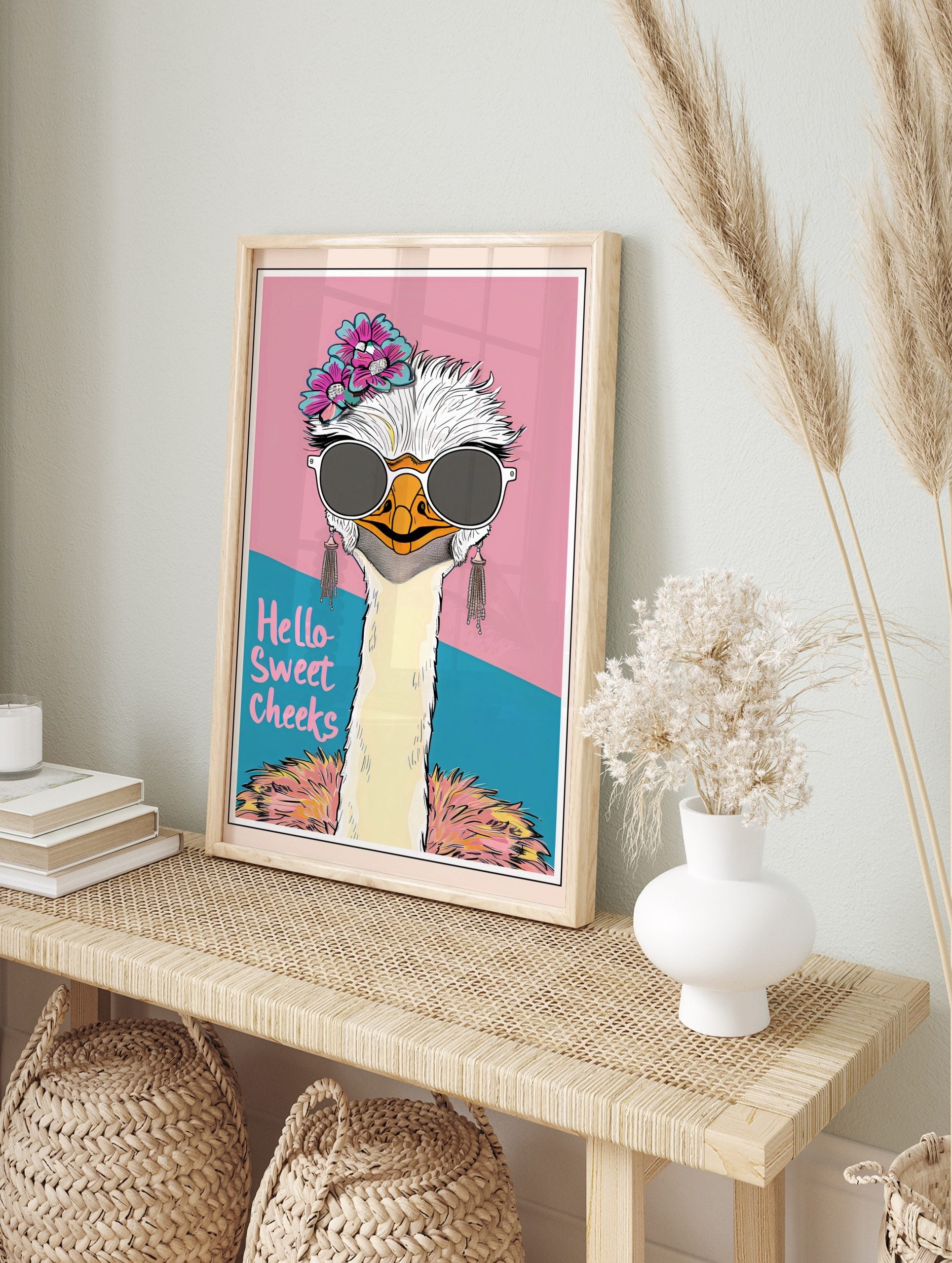 Quirky ostrich wall art wearing sunglasses and flowers, with 'Hello Sweet Cheeks' text on a pink and teal background, displayed as the same artwork in an alternate framed wall art mockup