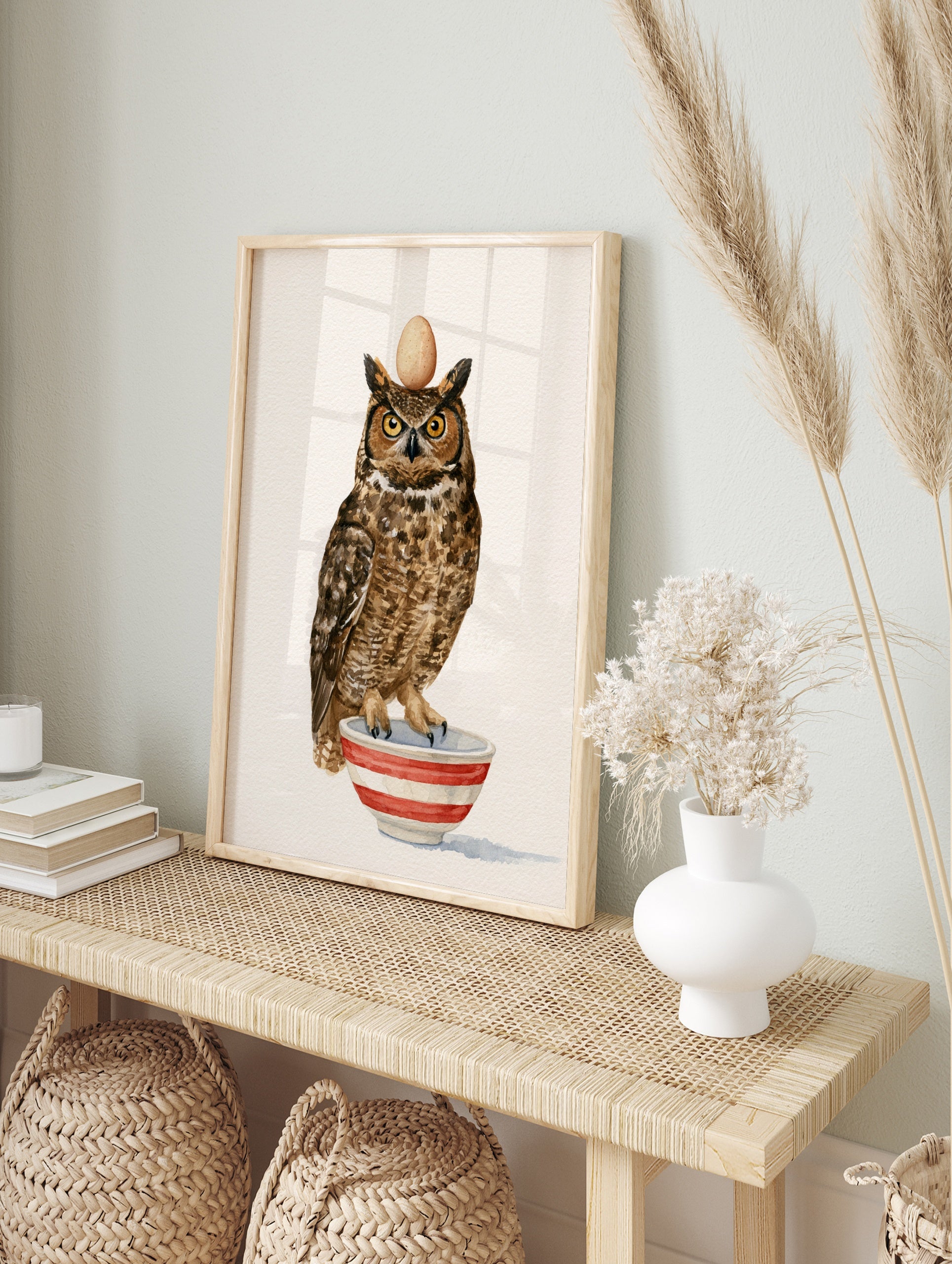 Watercolour illustration of a great horned owl balancing an egg on its head whilst standing, in an alternate framed mockup