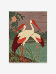 Two red-billed cranes with white bodies and red wings standing by a teal pond with green foliage