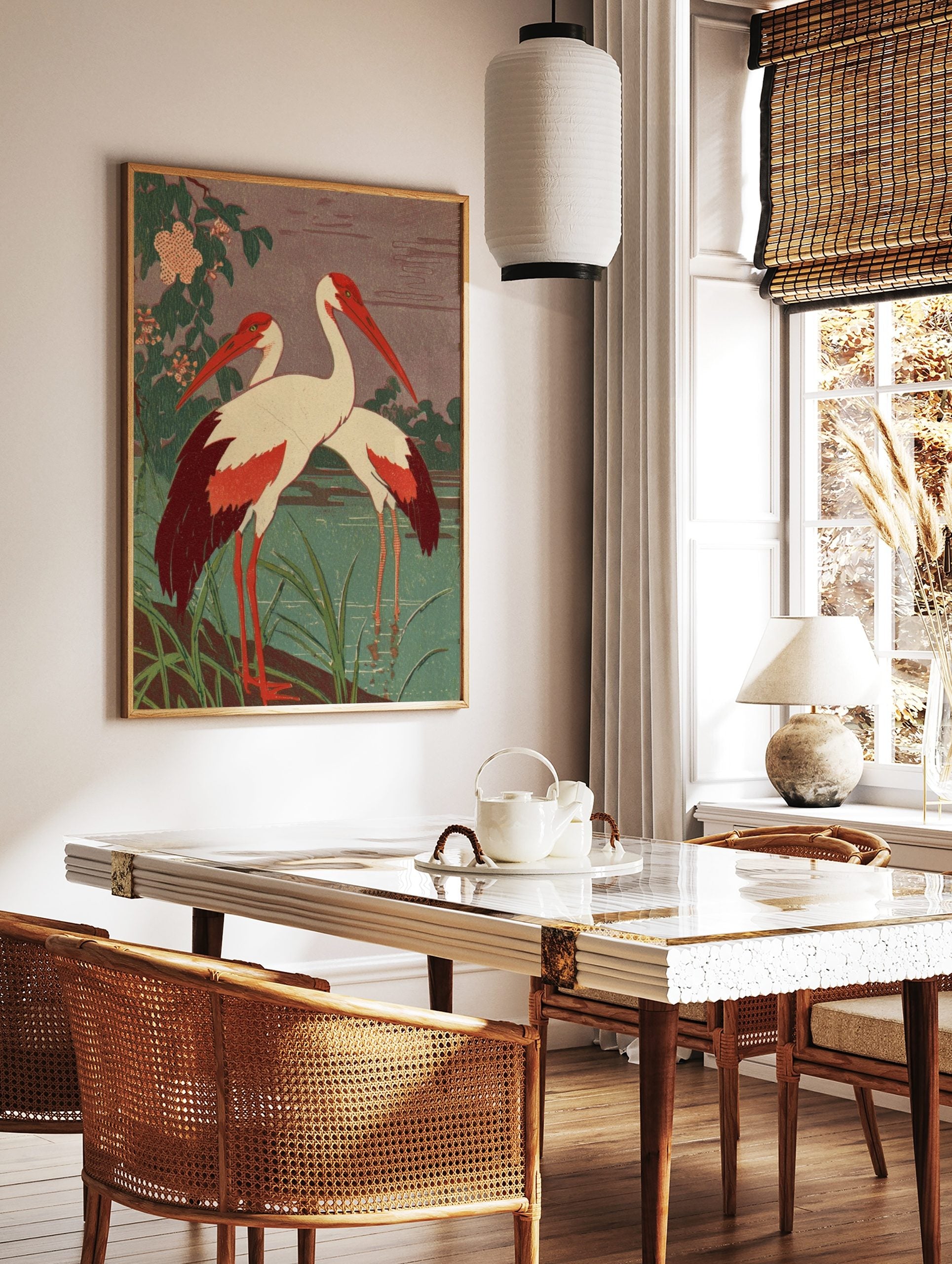 Two red-billed cranes with white bodies and red wings standing by a teal pond with green foliage, in a styled room mockup