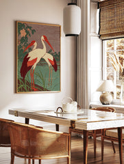 Two red-billed cranes with white bodies and red wings standing by a teal pond with green foliage, in a styled room mockup