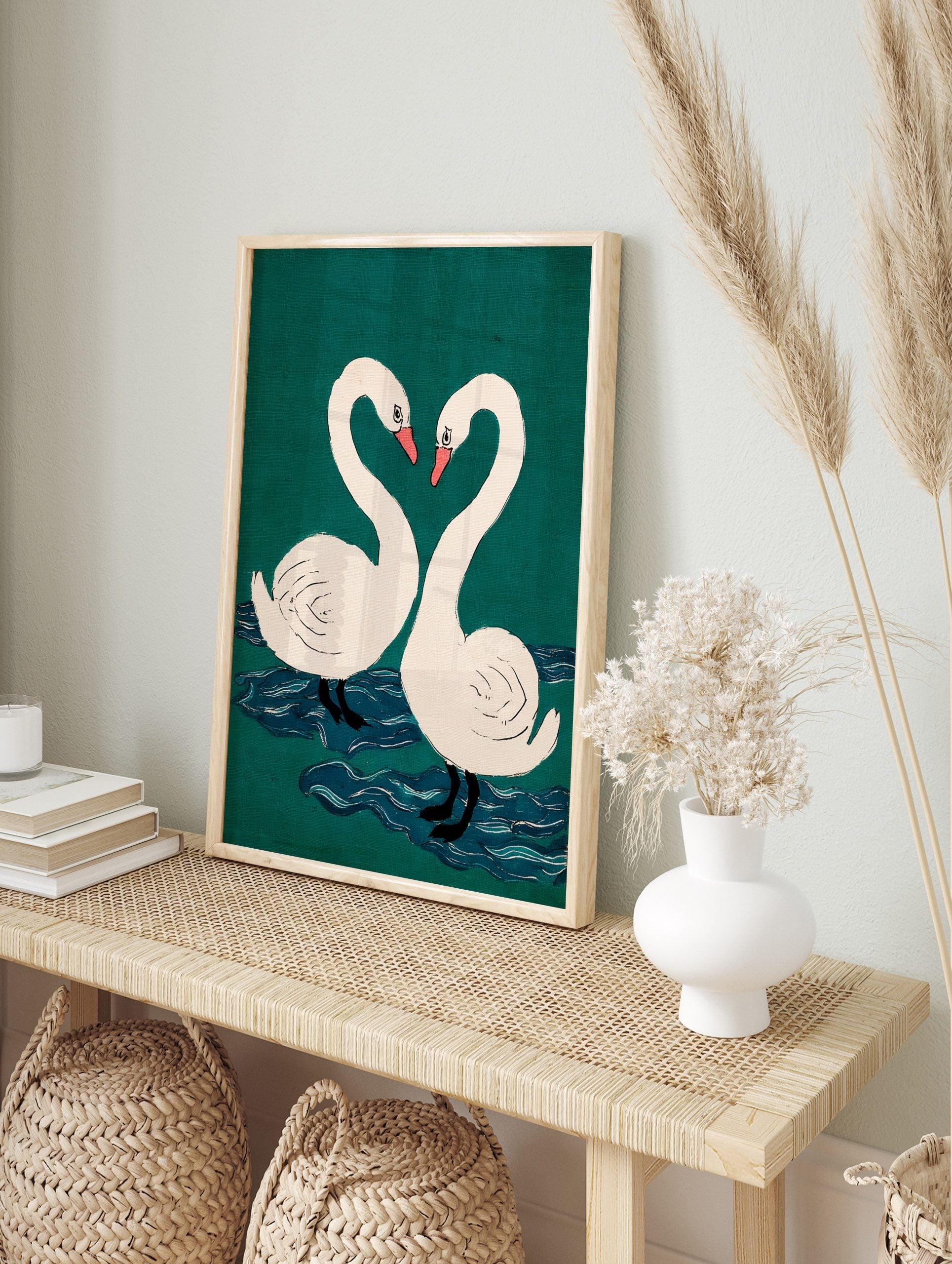 Two white swans with pink beaks form a heart shape against a teal-green background with blue, in an alternate framed mockup