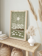 Pastoral sunburst landscape print with grazing sheep, mountains, clouds, and decorative, in an alternate framed mockup