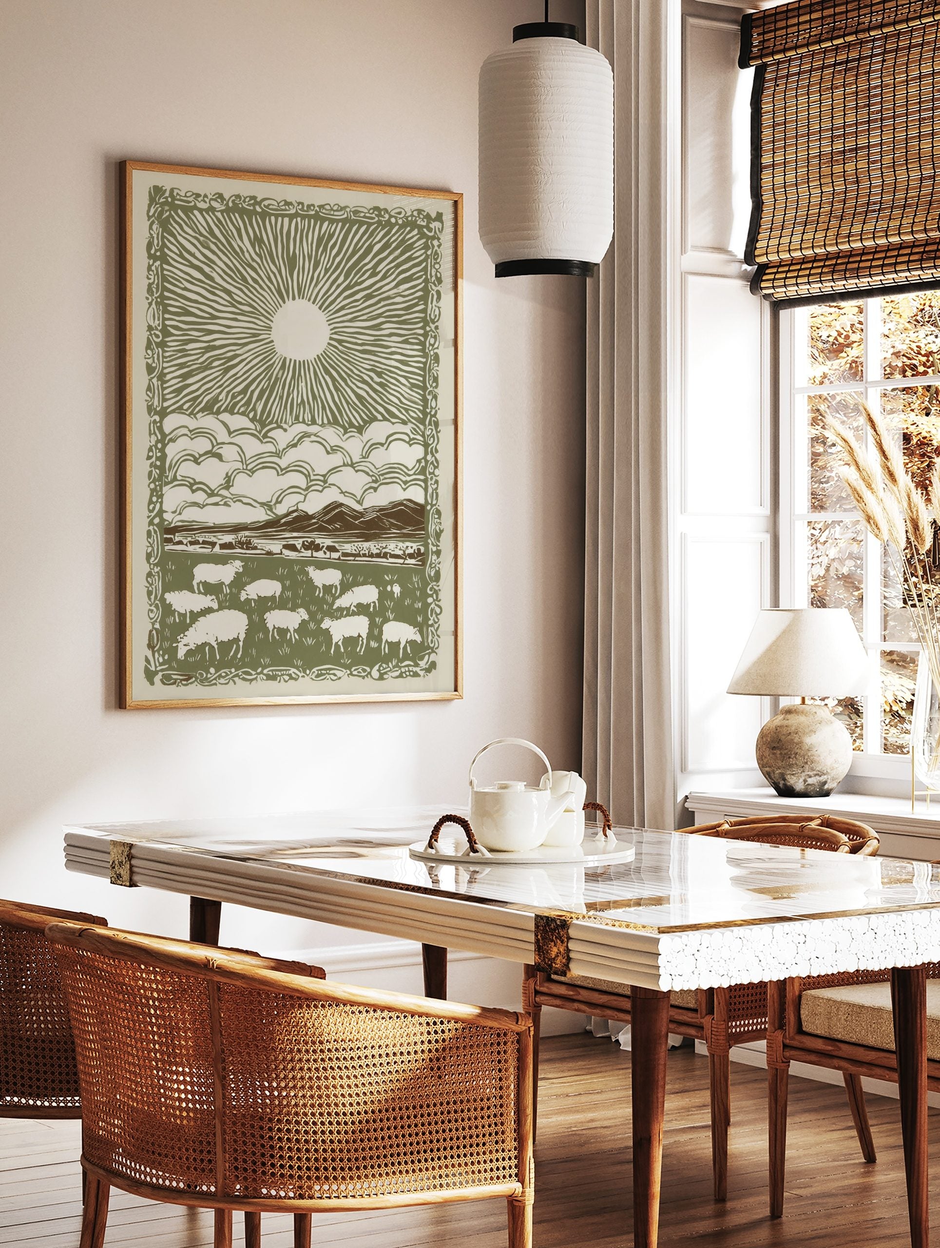 Pastoral sunburst landscape print with grazing sheep, mountains, clouds, and decorative border in, in a styled room mockup
