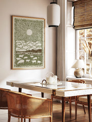 Pastoral sunburst landscape print with grazing sheep, mountains, clouds, and decorative border in, in a styled room mockup