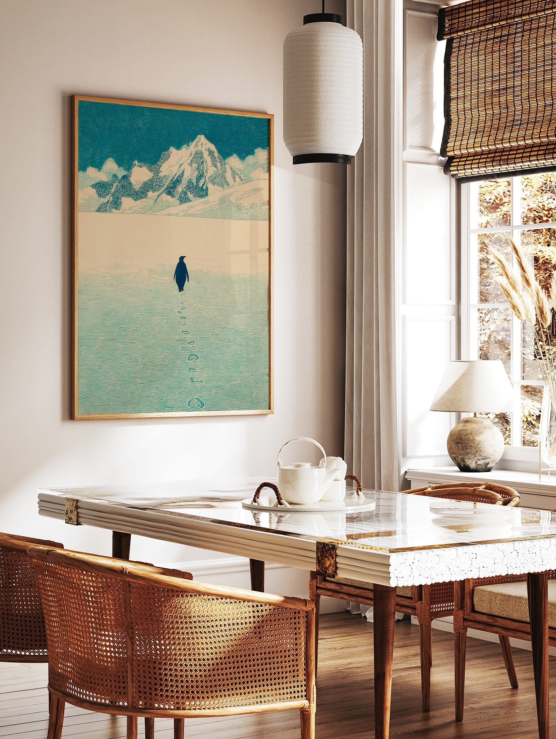 Illustrative print of a penguin walking on textured ice towards snow mountains under a blue sky, in a styled room mockup