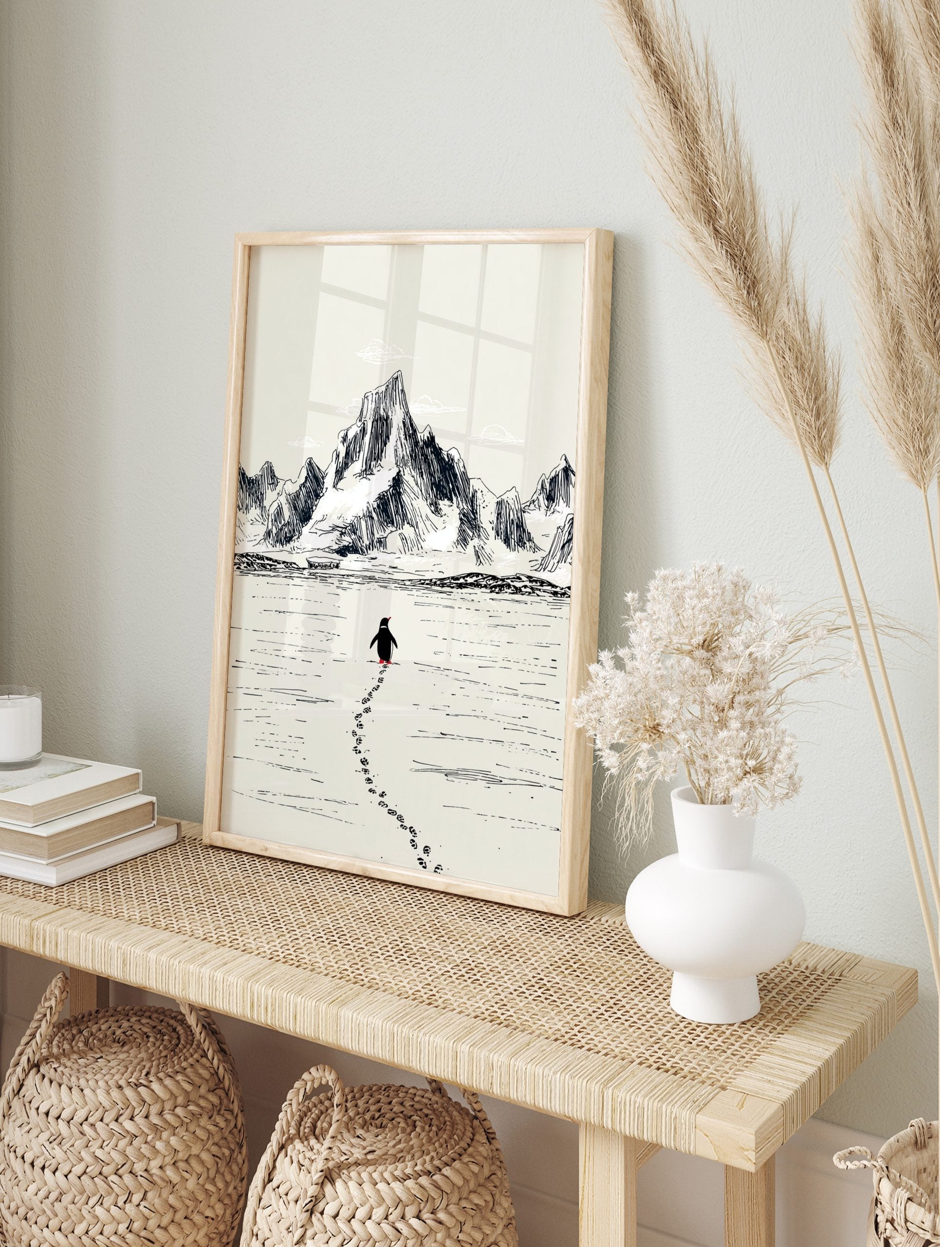 Sketch illustration of a penguin walking on ice, leaving footprints, with large mountains in, in an alternate framed mockup