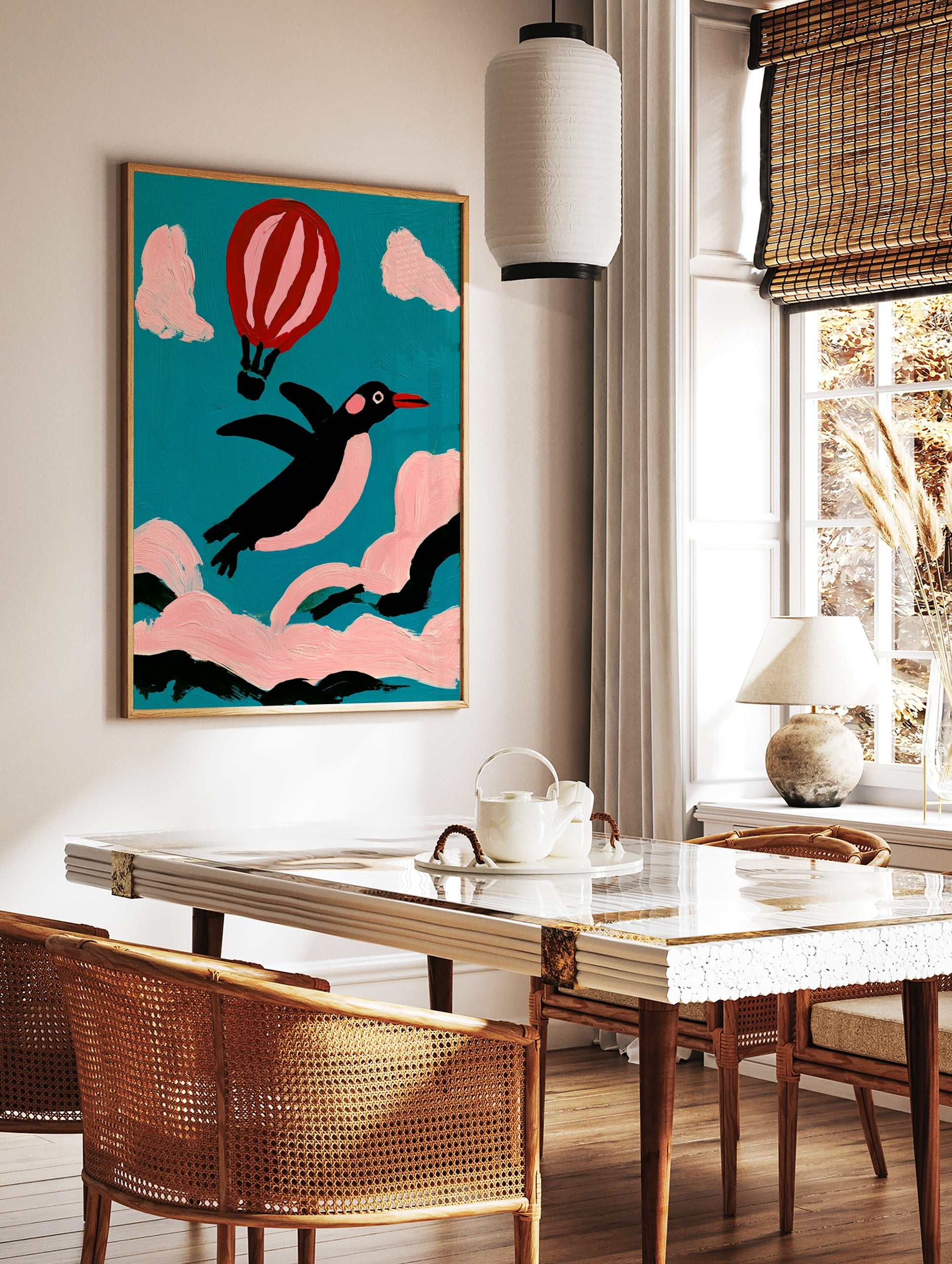 Whimsical illustration of a black penguin flying with a pink hot air balloon against a teal sky and, in a styled room mockup