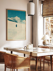 Illustrative woodcut style print of a penguin walking in snow towards mountains under a blue sky, in a styled room mockup