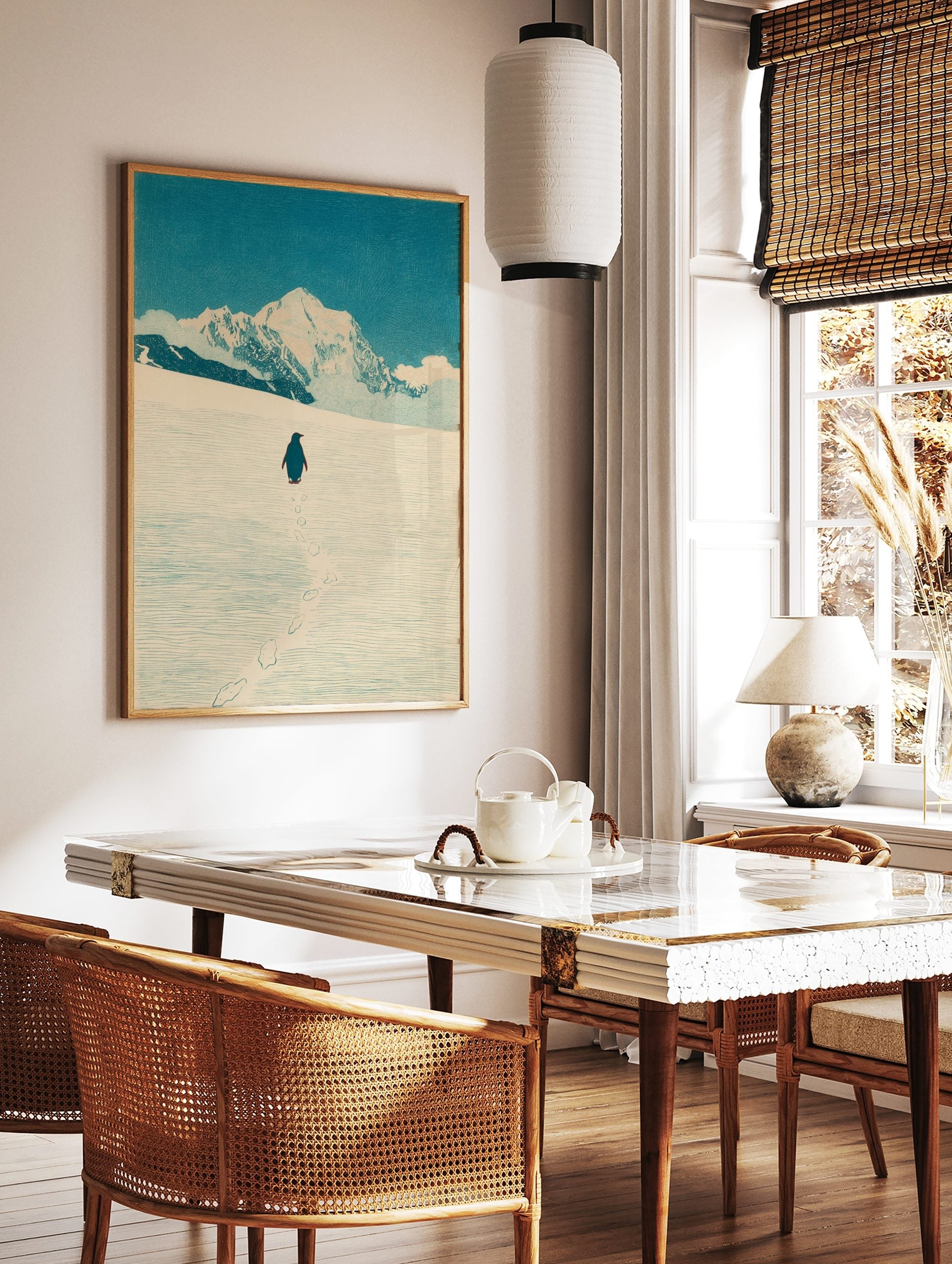 Illustrative print of a penguin walking in snow towards large, white mountains under a blue sky, in a styled room mockup
