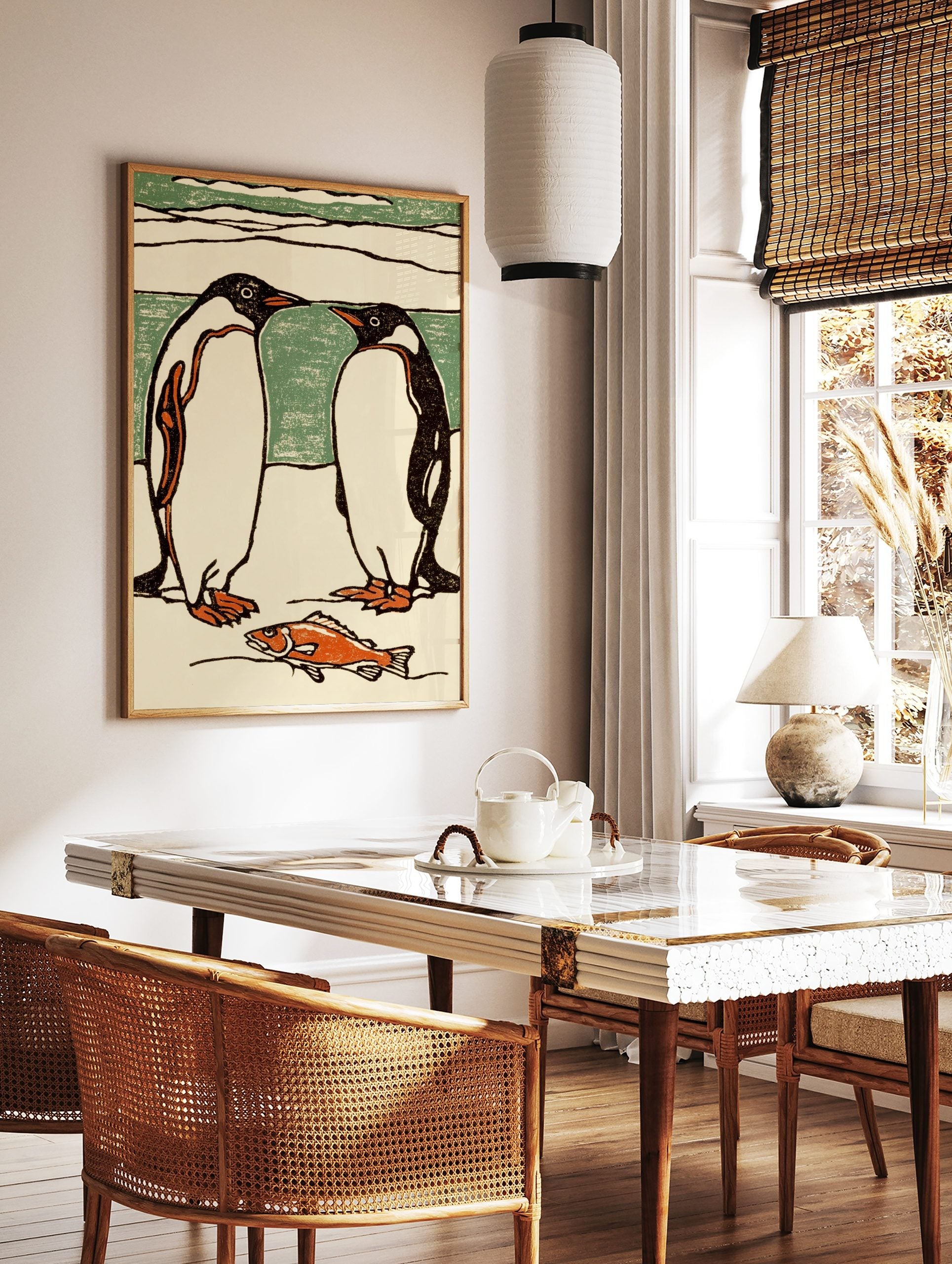 Illustrative print of two black and white penguins facing each other, with an orange fish on the ice, in a styled room mockup