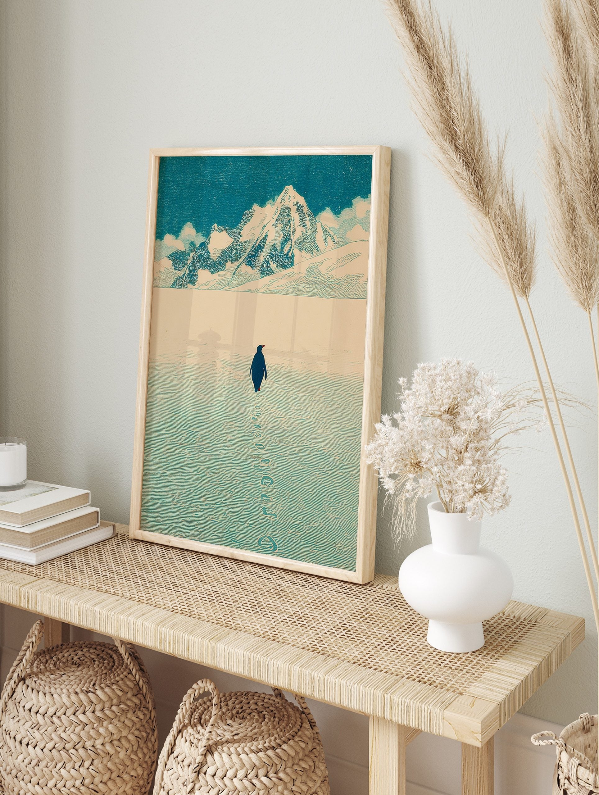 Illustrative print of a penguin walking on snow towards distant mountains under a blue sky, in an alternate framed mockup
