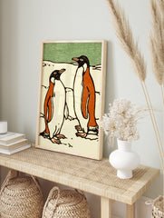 Illustrative print of two penguins in black, orange, and white on snow with a green background, in an alternate framed mockup