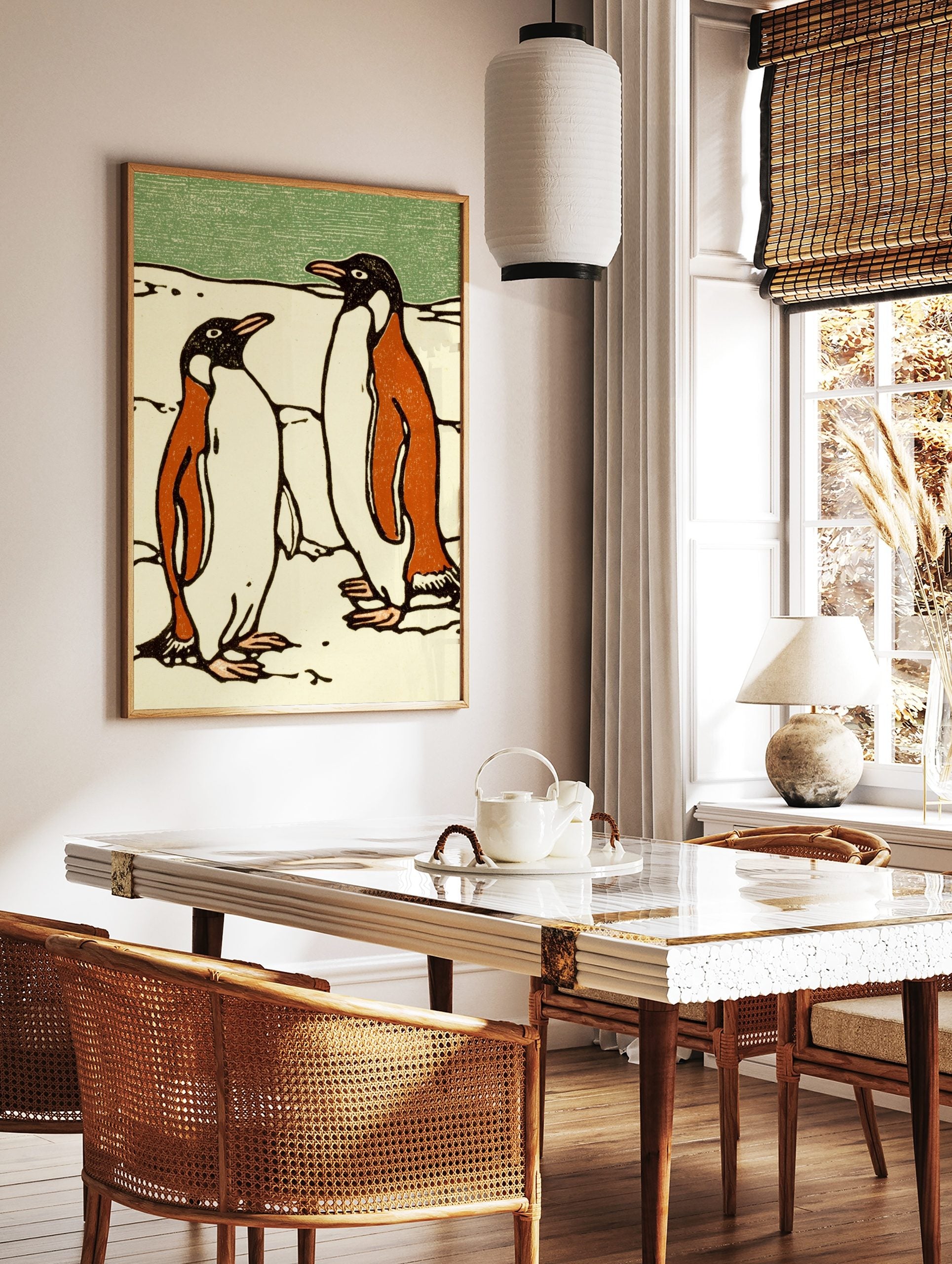 Illustrative print of two penguins in black, orange, and white on snow with a green background, in a styled room mockup