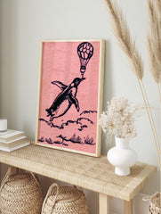 Whimsical black ink illustration of a penguin flying while holding a hot air balloon on a, in an alternate framed mockup