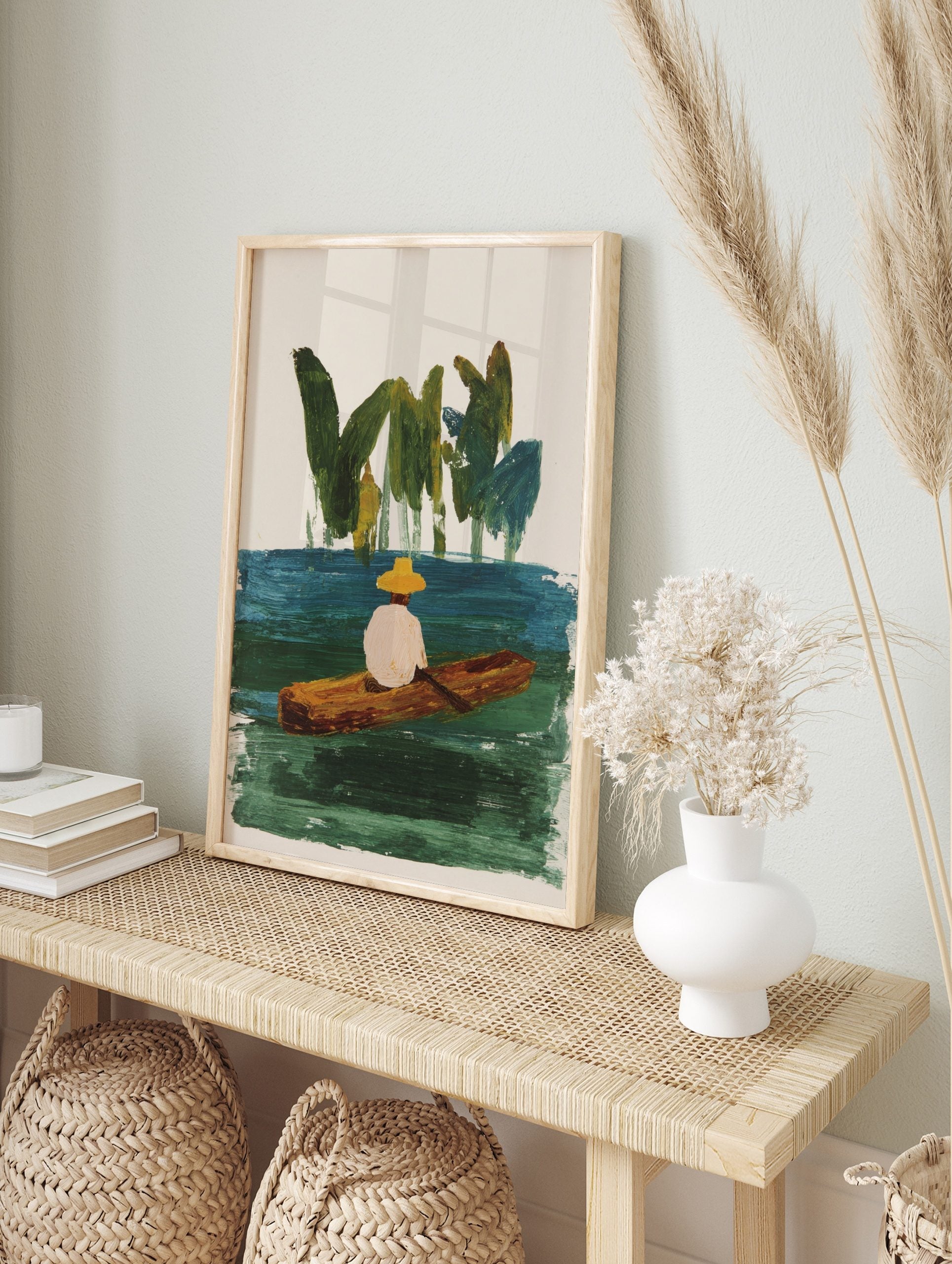 Illustrative painting of person in yellow hat in wooden boat on green-blue water with green, in an alternate framed mockup