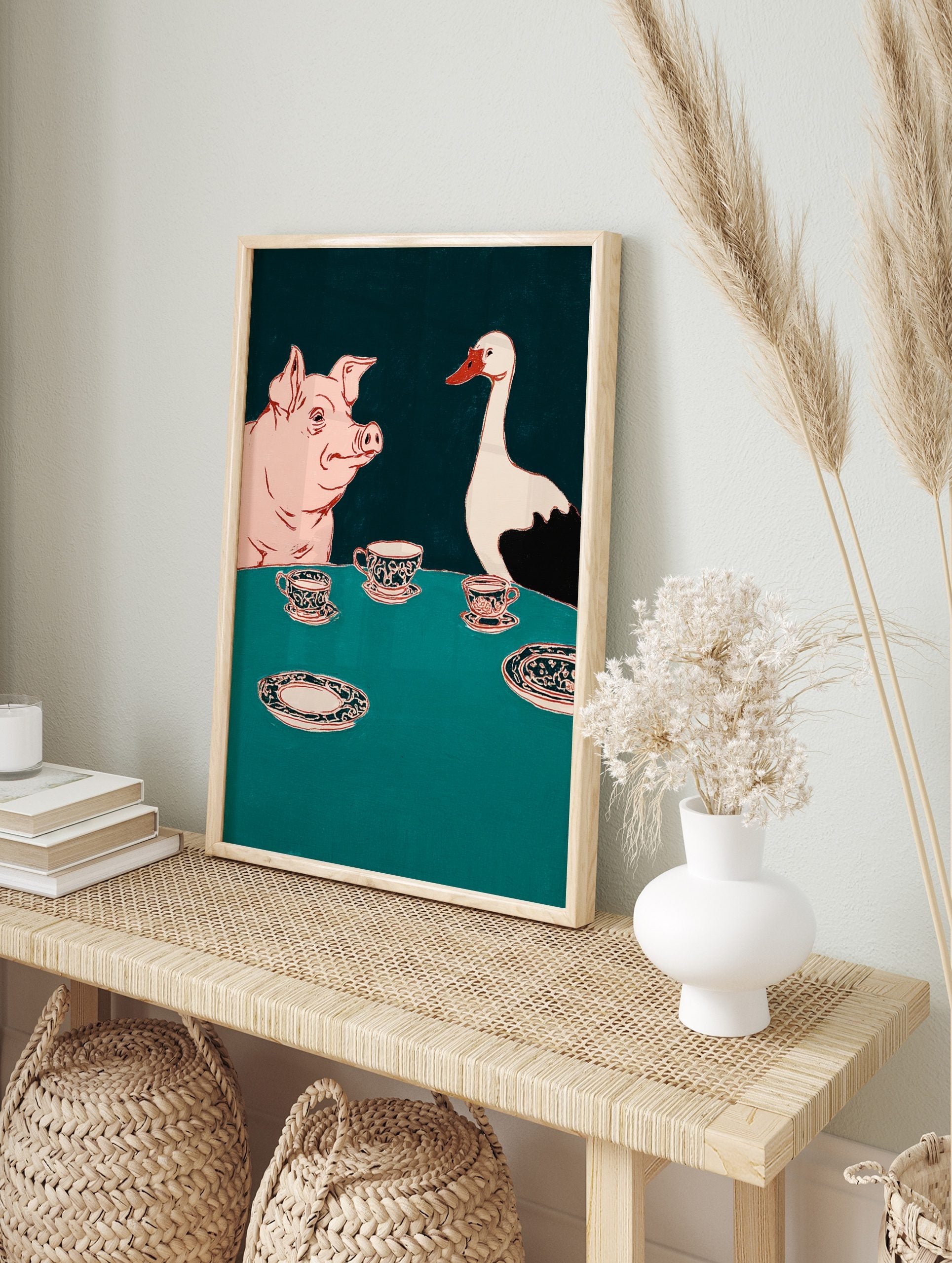 Illustrative wall art of a pink pig and white goose at a teal table with ornate teacups, in an alternate framed mockup