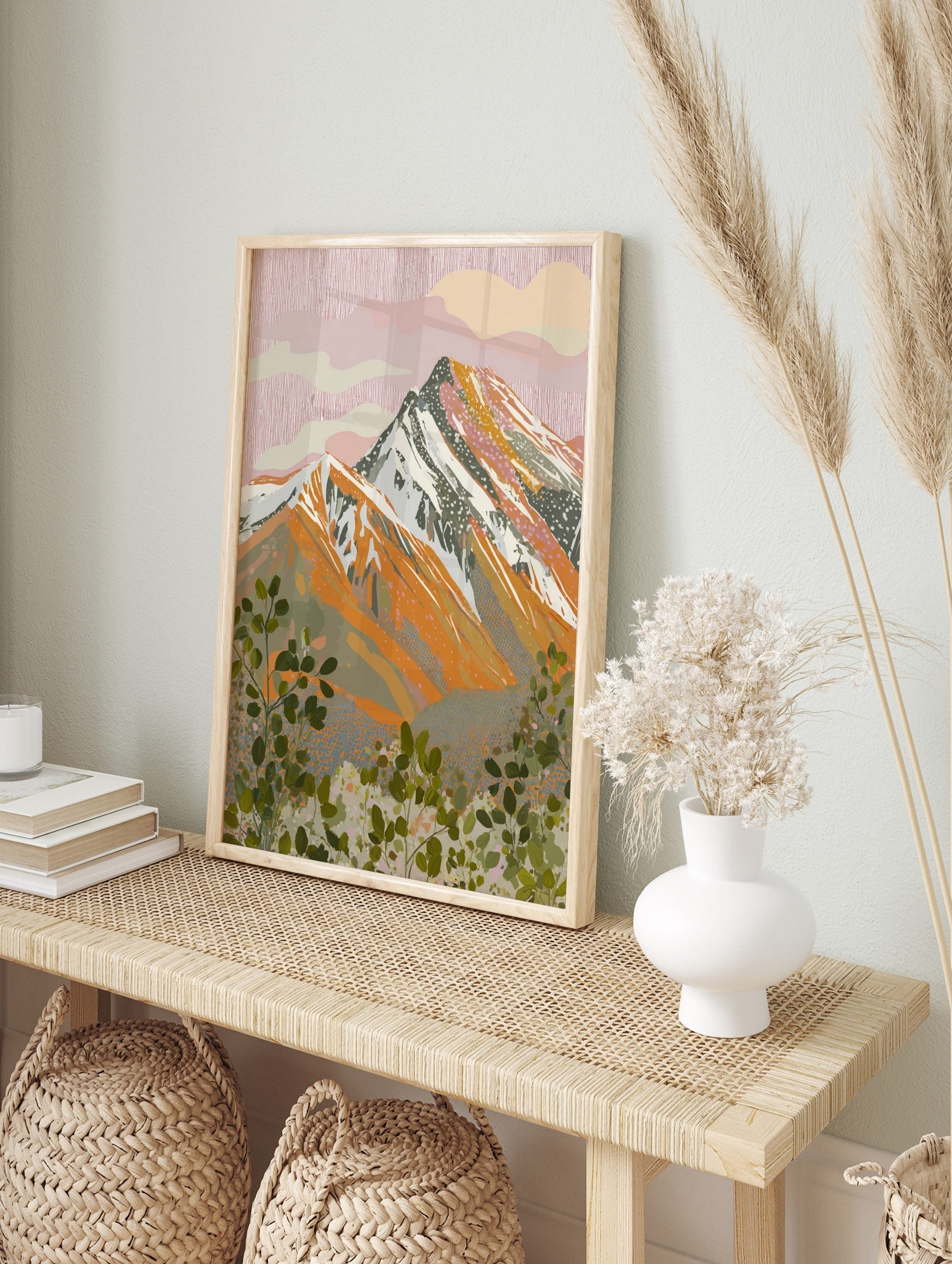 Illustrative mountain landscape print with pink sky, orange peaks, and green foliage, in an alternate framed mockup