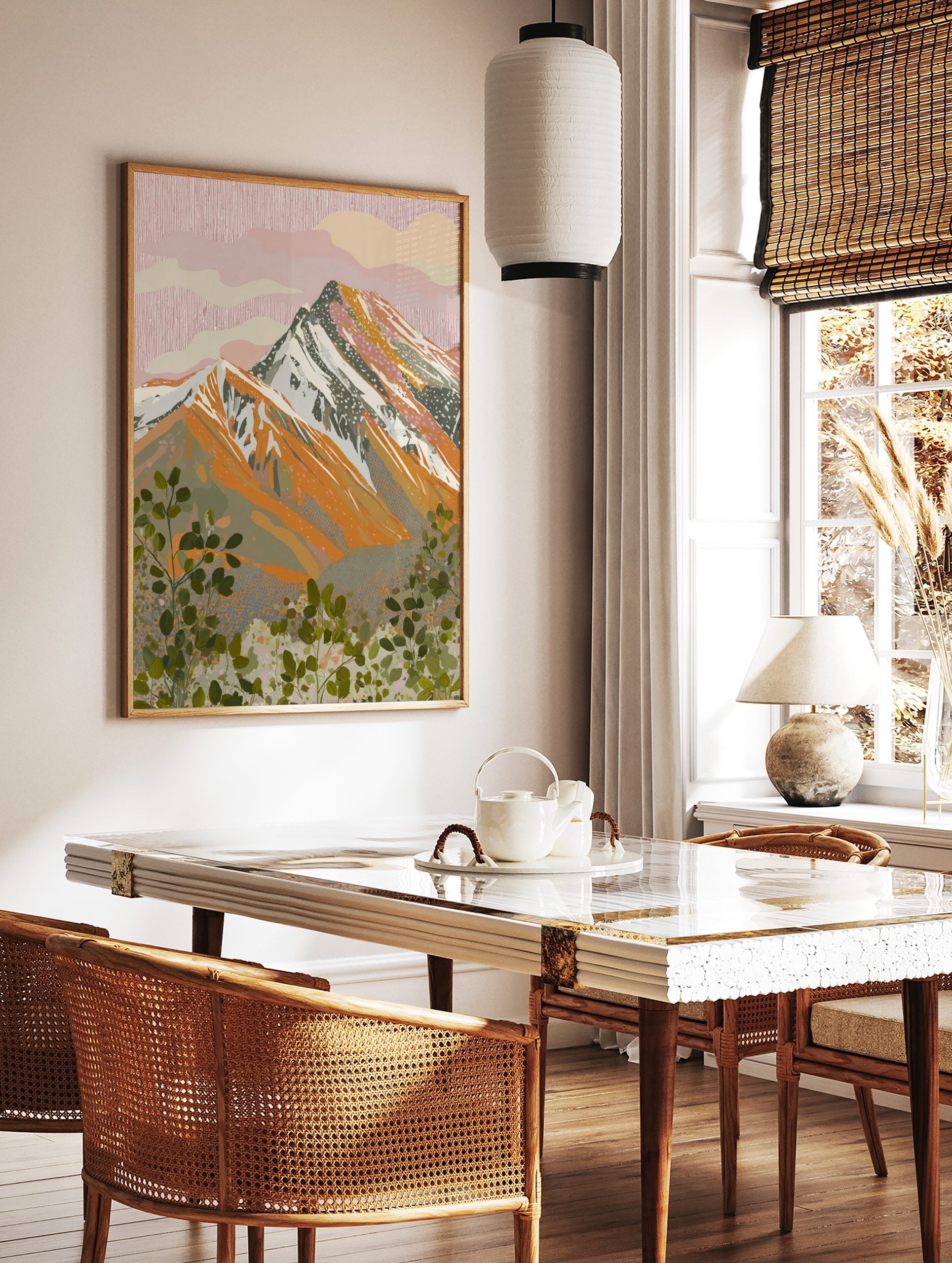 Illustrative mountain landscape print with pink sky, orange peaks, and green foliage foreground, in a styled room mockup