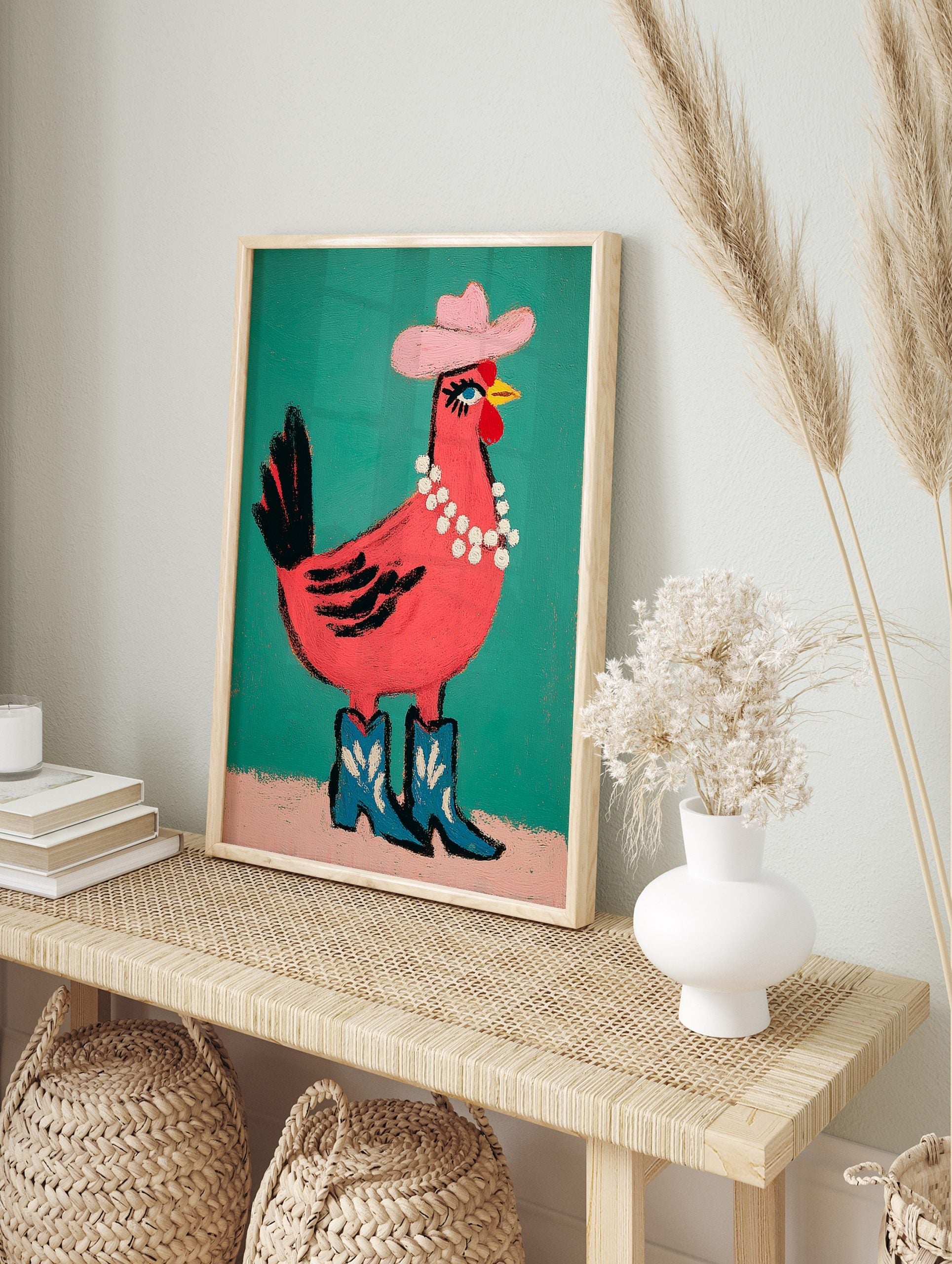 Pink chicken illustration wearing a pink cowboy hat, pearl necklace, and blue cowboy boots on, in an alternate framed mockup