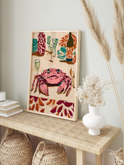 Illustrative wall art print of a pink crab at a dinner table with teal plates, glasses, and a, in an alternate framed mockup
