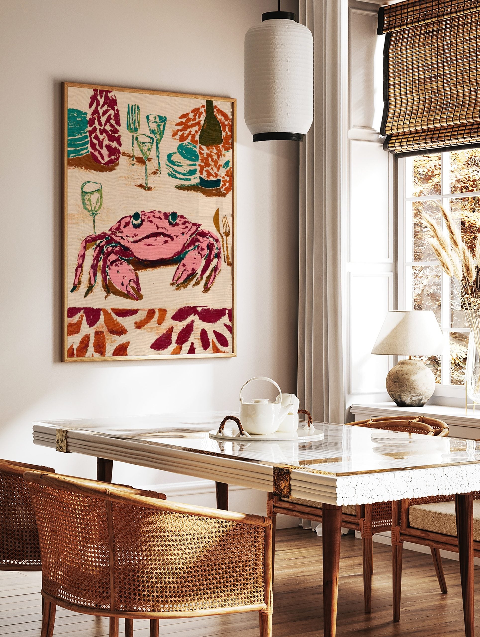 Illustrative wall art print of a pink crab at a dinner table with teal plates, glasses, and a wine, in a styled room mockup