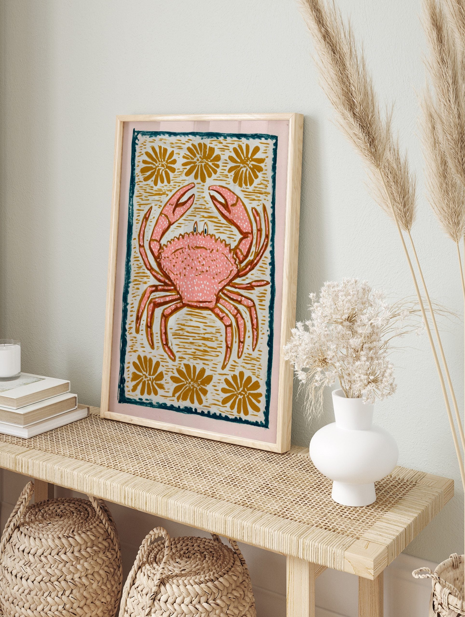 Pink crab illustration with white speckles, golden flowers, and a dark teal border on a light, in an alternate framed mockup