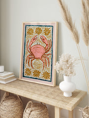 Pink crab illustration with white speckles, golden flowers, and a dark teal border on a light, in an alternate framed mockup