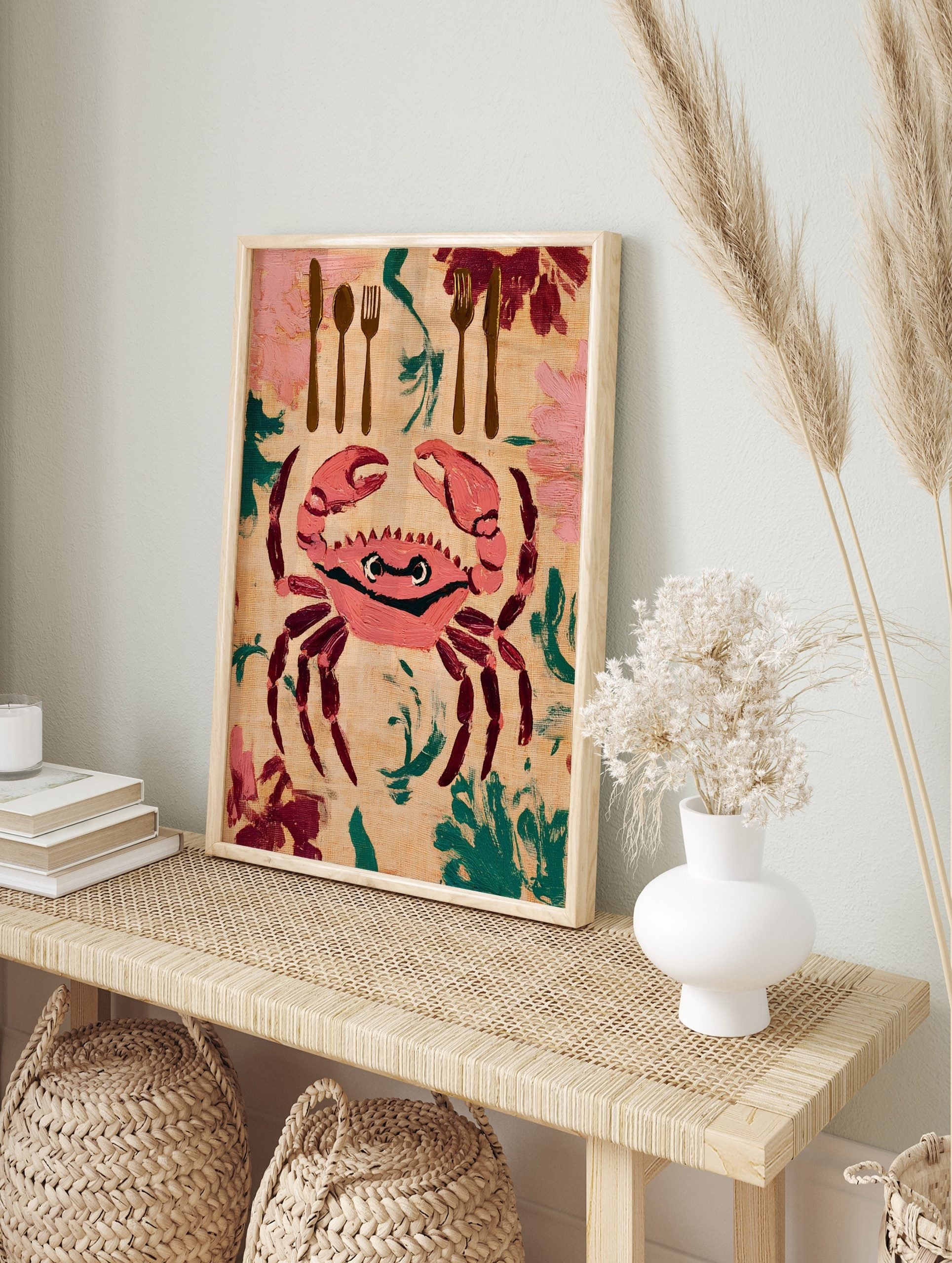 Illustrative wall art print of a pink crab with cutlery and foliage on a beige background, in an alternate framed mockup