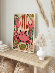 Pink crab illustration with brown cutlery (forks, spoon) and green bowl on beige background, in an alternate framed mockup