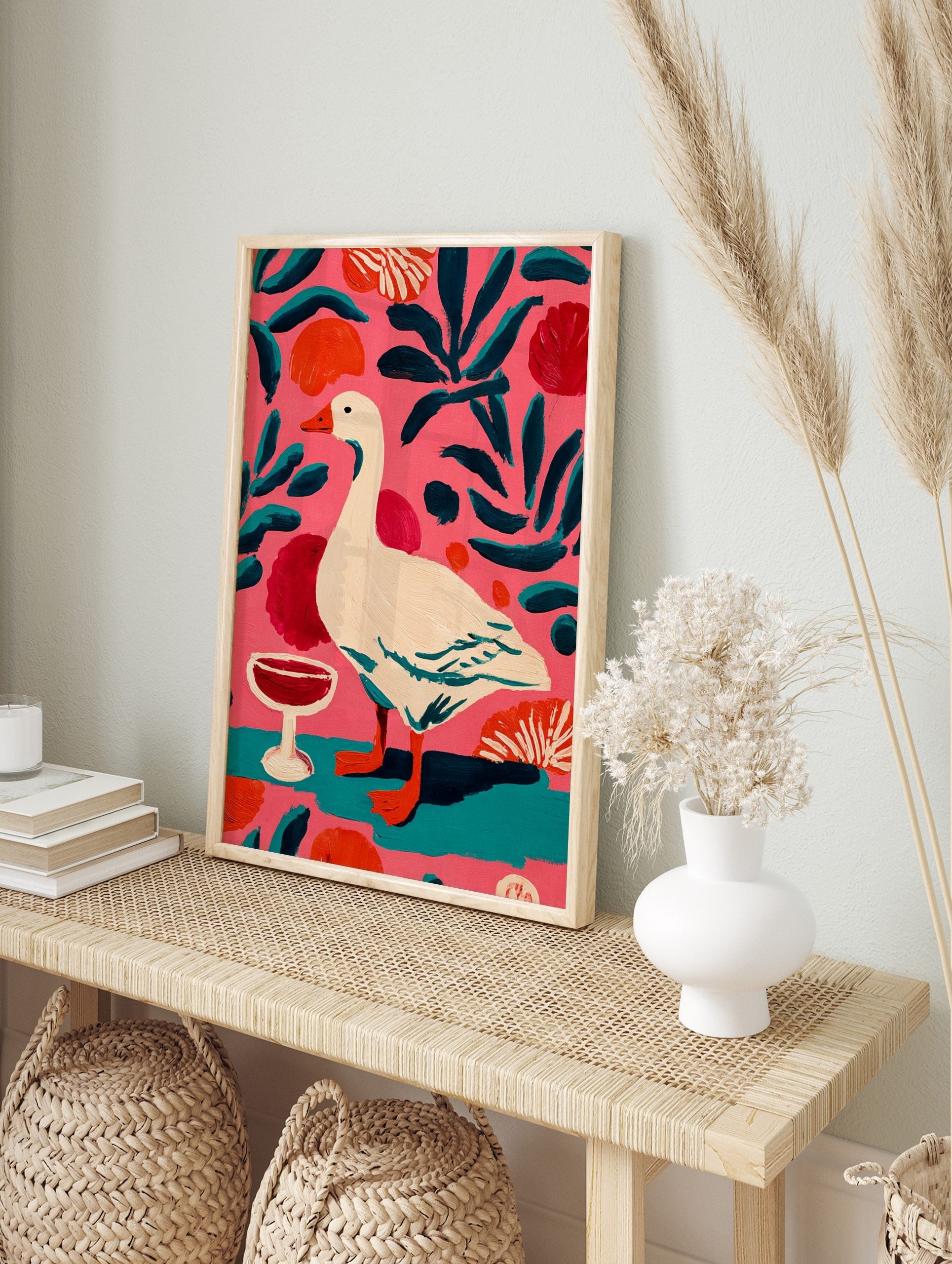 Illustrative painting of a white goose with orange beak, red wine glass, and teal leaves on a, in an alternate framed mockup